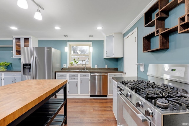 kitchen with light wood-type flooring, ornamental molding, a sink, dark countertops, and appliances with stainless steel finishes