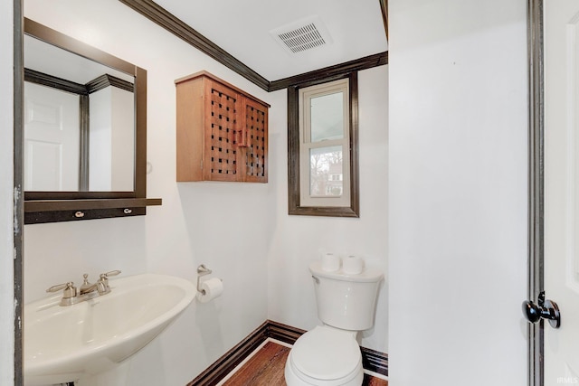 half bathroom with visible vents, toilet, a sink, crown molding, and baseboards