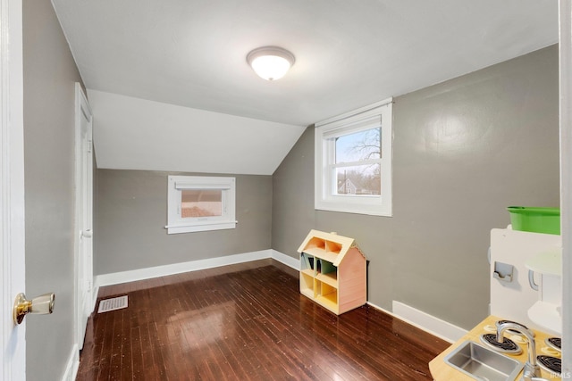 additional living space featuring dark wood-style floors, baseboards, visible vents, lofted ceiling, and a sink