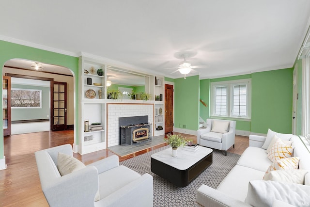 living room featuring baseboards, ornamental molding, wood finished floors, arched walkways, and a ceiling fan