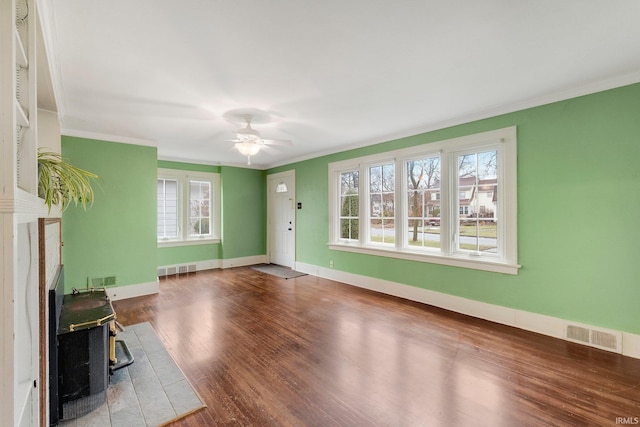 unfurnished living room featuring a wealth of natural light, wood finished floors, a wood stove, and ornamental molding