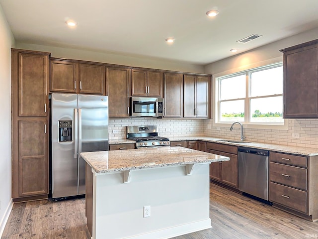 kitchen with visible vents, a kitchen island, light wood-style flooring, stainless steel appliances, and a sink