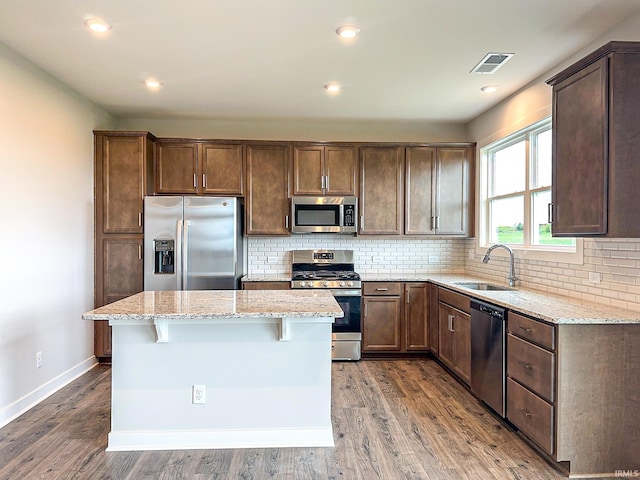 kitchen with a sink, light stone counters, tasteful backsplash, wood finished floors, and stainless steel appliances