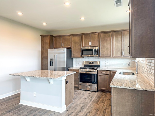 kitchen featuring a kitchen island, a sink, stainless steel appliances, dark wood-type flooring, and backsplash