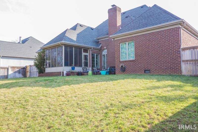 rear view of property featuring a chimney, fence, a yard, and a sunroom