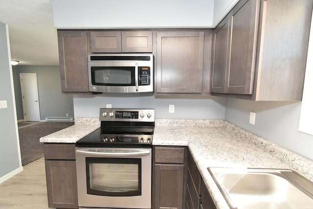 kitchen with light wood-style flooring, a sink, dark brown cabinets, appliances with stainless steel finishes, and a baseboard heating unit