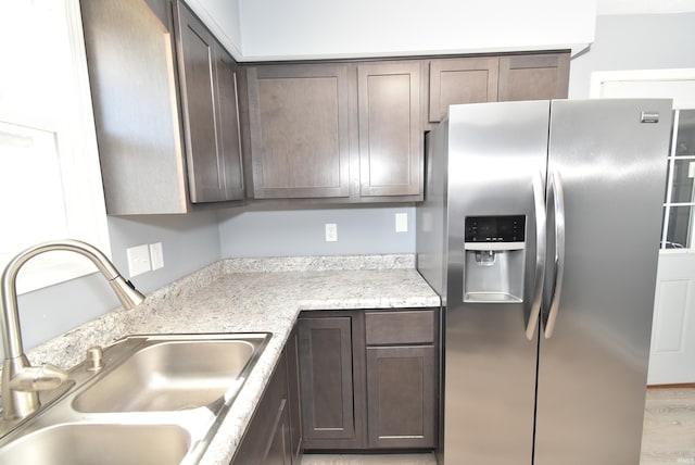 kitchen featuring a sink, light wood-style floors, dark brown cabinetry, stainless steel fridge with ice dispenser, and light countertops