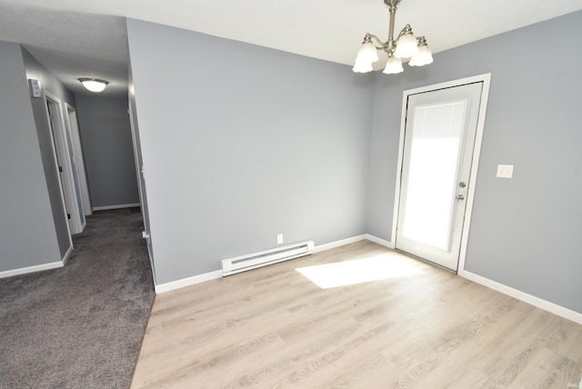 spare room featuring baseboard heating, an inviting chandelier, baseboards, and wood finished floors