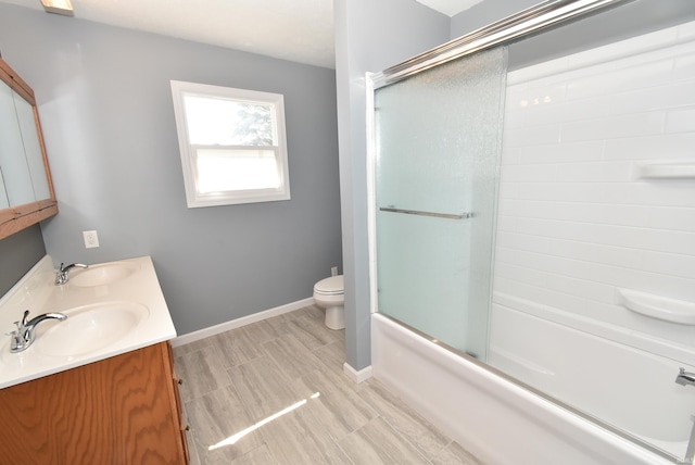 bathroom with a sink, baseboards, toilet, and shower / bath combination with glass door