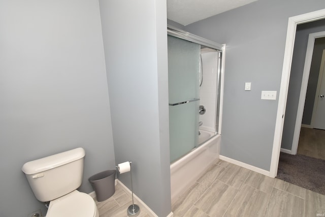 full bath featuring baseboards, toilet, and shower / bath combination with glass door