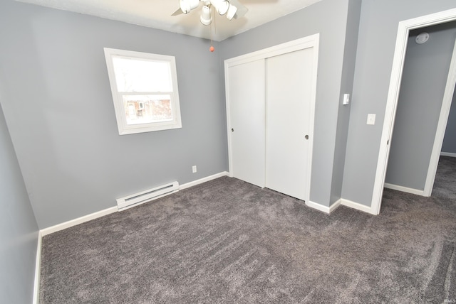 unfurnished bedroom with dark colored carpet, a baseboard heating unit, baseboards, and a closet