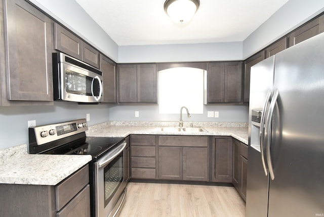 kitchen with dark brown cabinets, light countertops, light wood-type flooring, appliances with stainless steel finishes, and a sink