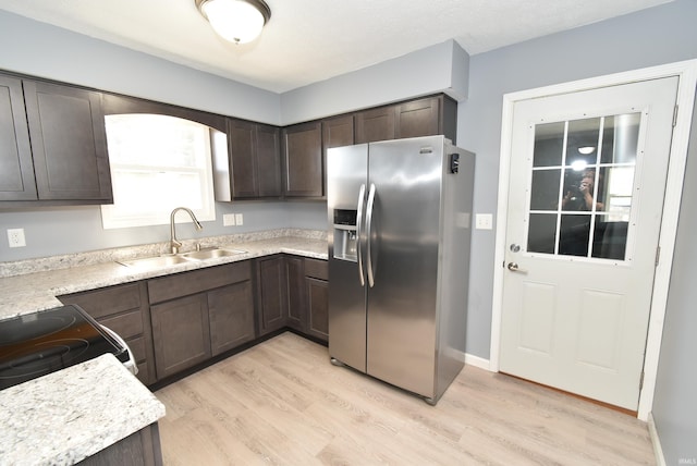 kitchen featuring dark brown cabinets, light countertops, light wood-style floors, stainless steel fridge, and a sink