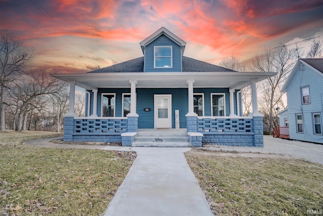 bungalow-style home with roof with shingles, a porch, and a front lawn