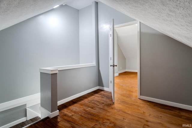 bonus room featuring baseboards, a textured ceiling, wood finished floors, and vaulted ceiling