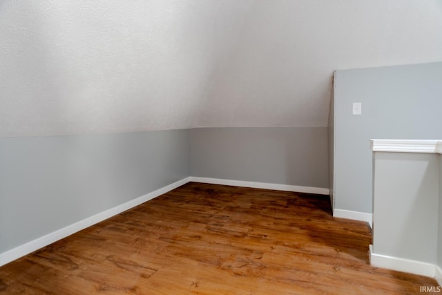 additional living space with lofted ceiling, wood finished floors, baseboards, and a textured ceiling