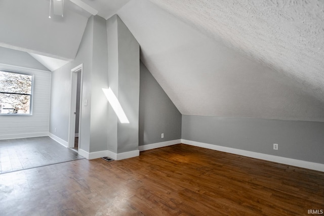 bonus room with a ceiling fan, wood finished floors, baseboards, visible vents, and vaulted ceiling