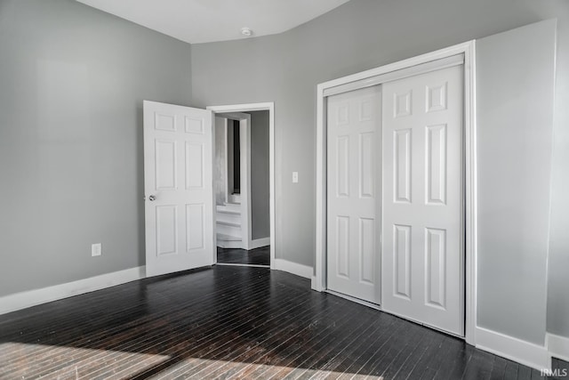 unfurnished bedroom with dark wood-type flooring, baseboards, and a closet