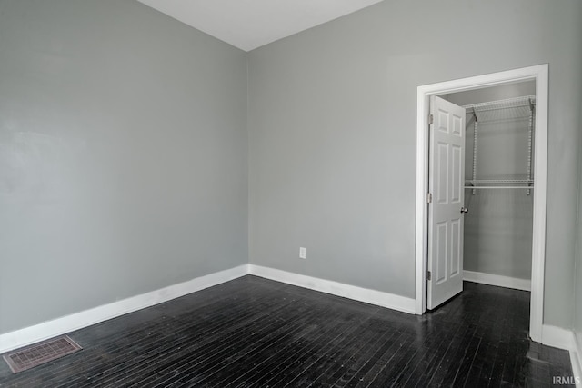 unfurnished bedroom with visible vents, baseboards, dark wood-type flooring, and a closet