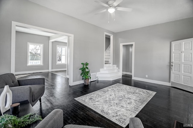 living area featuring visible vents, dark wood-style floors, baseboards, ceiling fan, and stairs