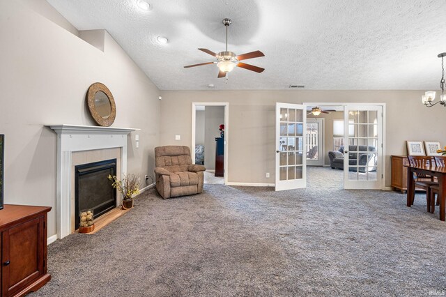 carpeted living room featuring lofted ceiling, french doors, a textured ceiling, a tiled fireplace, and ceiling fan with notable chandelier