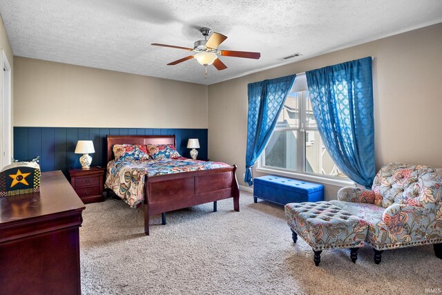 bedroom with visible vents, a wainscoted wall, carpet floors, a textured ceiling, and a ceiling fan