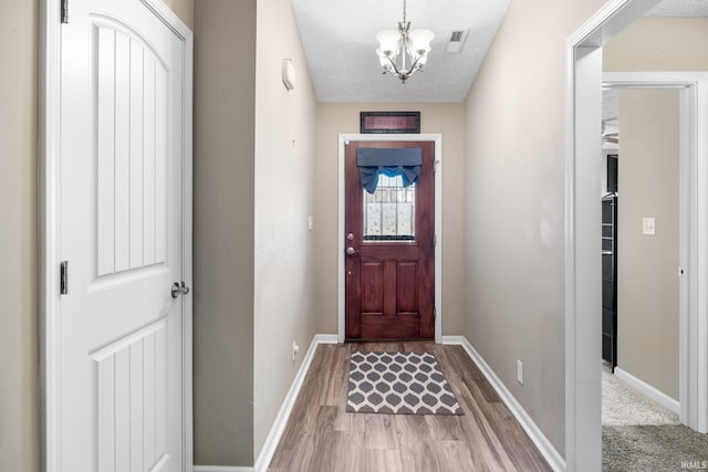 entrance foyer with wood finished floors, visible vents, baseboards, a textured ceiling, and a notable chandelier