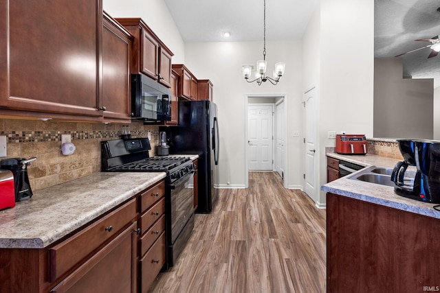 kitchen featuring baseboards, light wood-type flooring, decorative backsplash, ceiling fan with notable chandelier, and black appliances