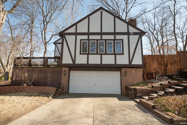 tudor-style house featuring stucco siding, driveway, an attached garage, brick siding, and a chimney