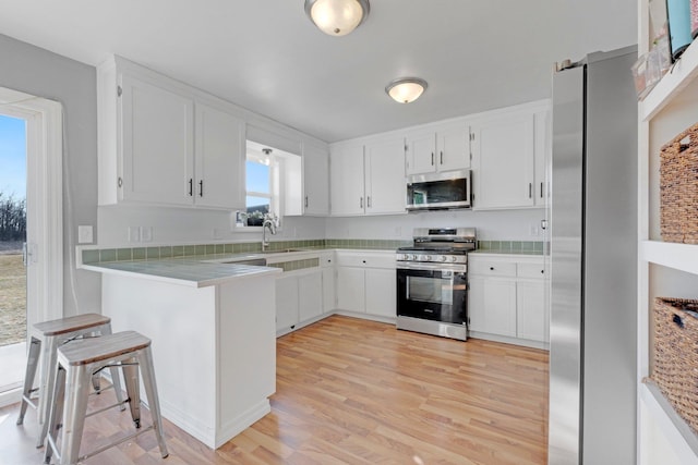 kitchen featuring light wood-type flooring, light countertops, stainless steel appliances, white cabinetry, and a sink