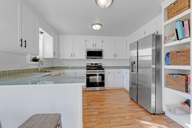 kitchen featuring tile countertops, a peninsula, white cabinets, stainless steel appliances, and a sink