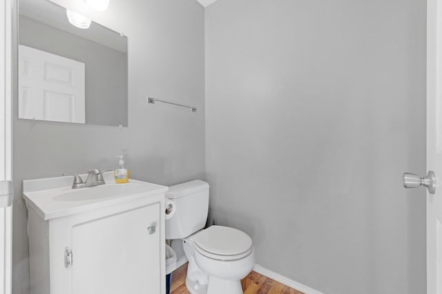 half bath featuring vanity, toilet, wood finished floors, and baseboards