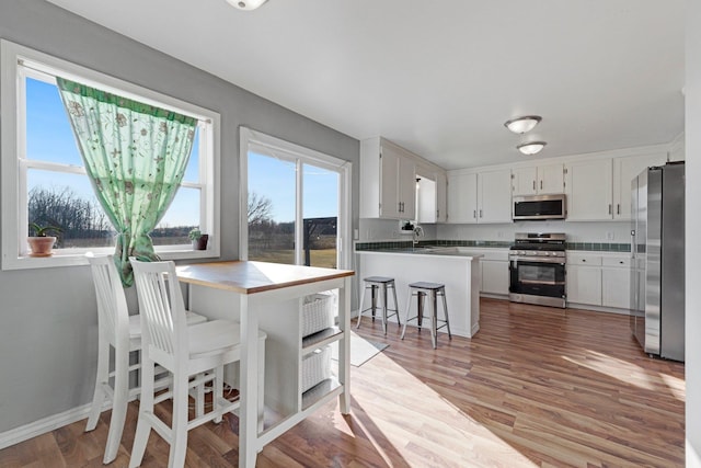 kitchen featuring white cabinetry, appliances with stainless steel finishes, a peninsula, and light wood finished floors