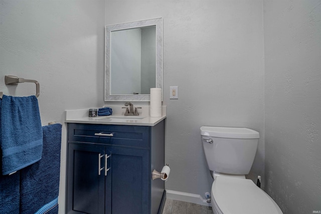 half bath featuring baseboards, toilet, wood finished floors, and vanity