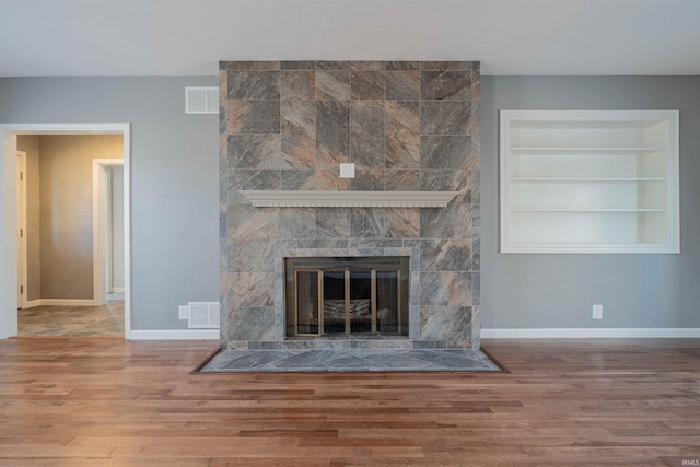 interior details featuring visible vents, baseboards, wood finished floors, and a tile fireplace