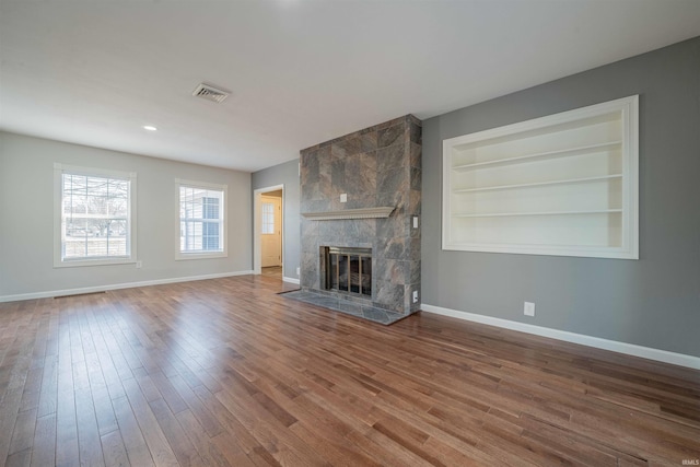 unfurnished living room with wood finished floors, a fireplace, visible vents, and baseboards