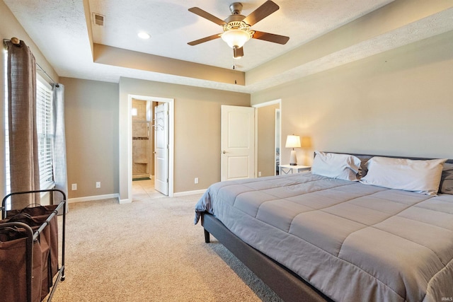 bedroom featuring visible vents, baseboards, a tray ceiling, light colored carpet, and connected bathroom