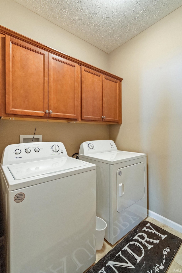 laundry room with washer and clothes dryer, cabinet space, a textured ceiling, and baseboards