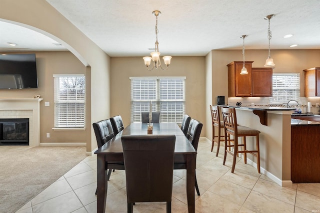 dining area featuring a textured ceiling, a glass covered fireplace, light tile patterned floors, baseboards, and light colored carpet