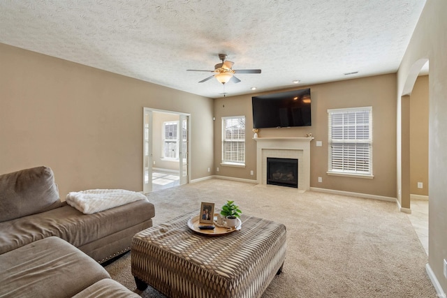 living area with a textured ceiling, carpet flooring, a fireplace, baseboards, and ceiling fan