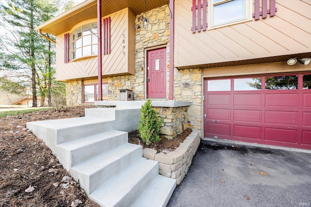 entrance to property featuring aphalt driveway, an attached garage, and stone siding