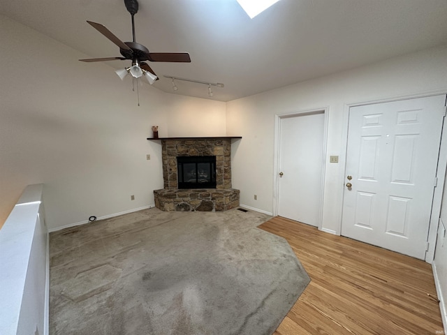 unfurnished living room with baseboards, ceiling fan, light wood-type flooring, rail lighting, and a fireplace