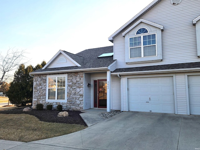 traditional home featuring an attached garage, stone siding, driveway, and roof with shingles