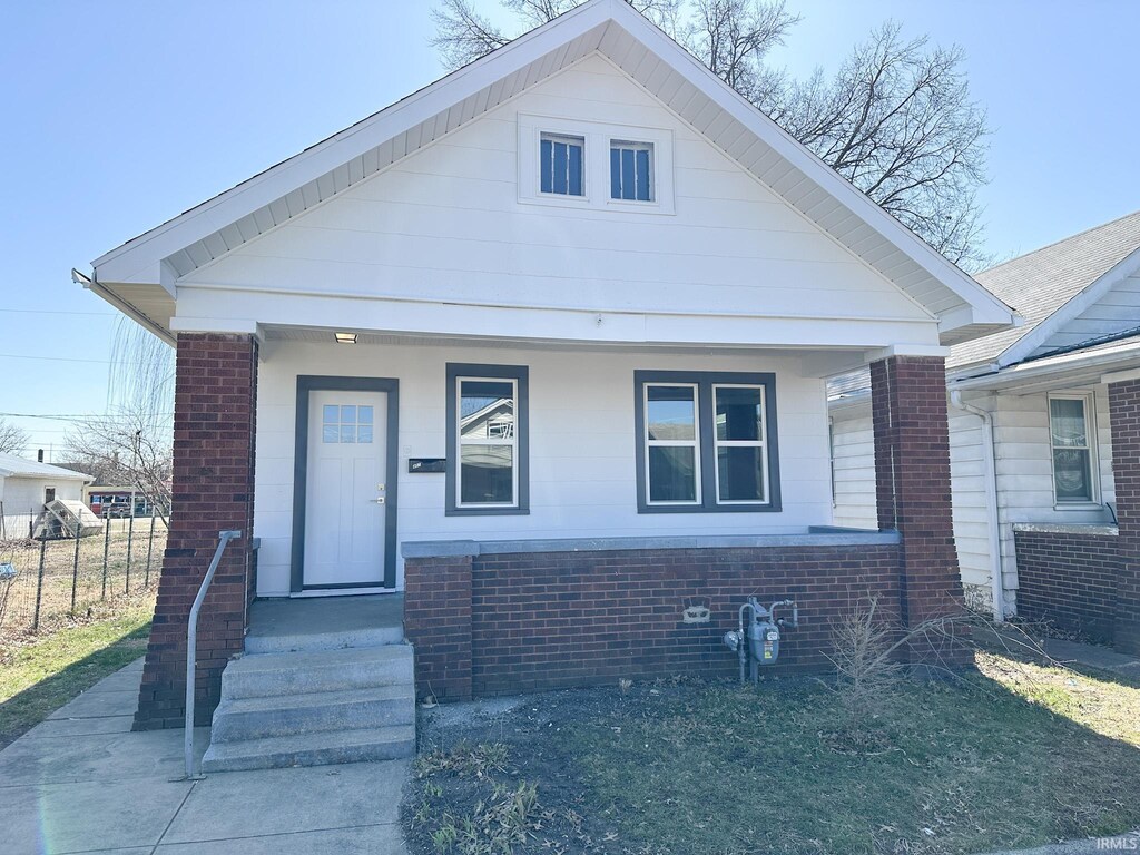 bungalow featuring brick siding, covered porch, and fence