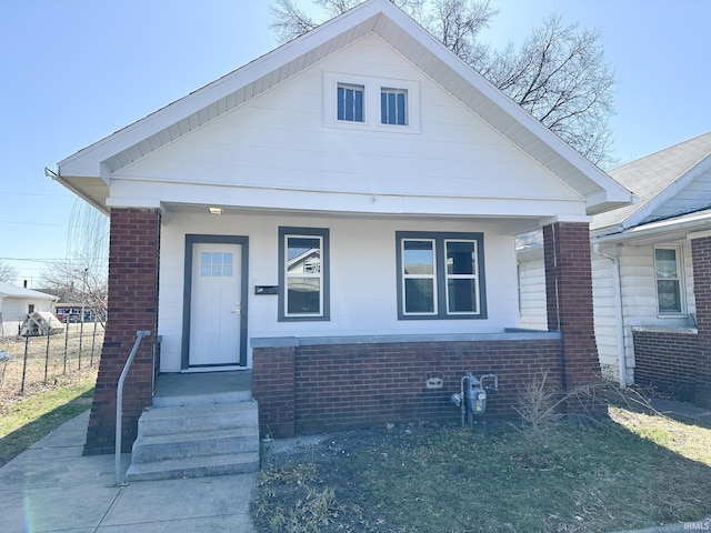 bungalow featuring brick siding, covered porch, and fence