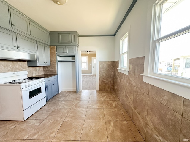 kitchen featuring white range with gas cooktop, ornamental molding, under cabinet range hood, green cabinets, and light tile patterned flooring