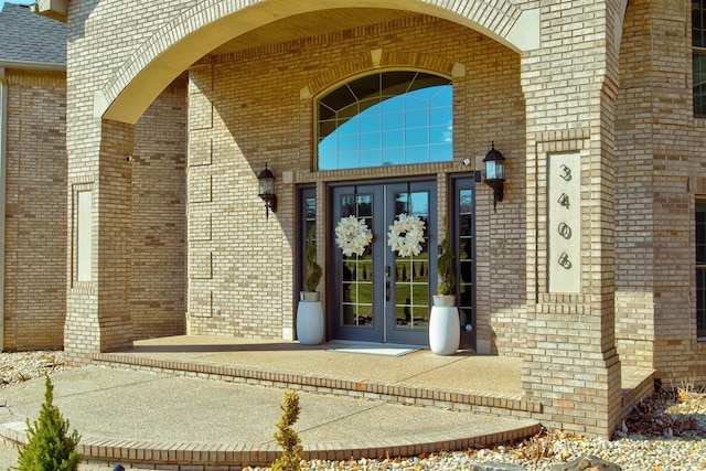 entrance to property featuring brick siding, french doors, and a shingled roof