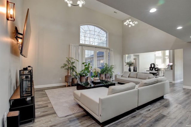 living area with baseboards, recessed lighting, light wood-style flooring, a high ceiling, and an inviting chandelier