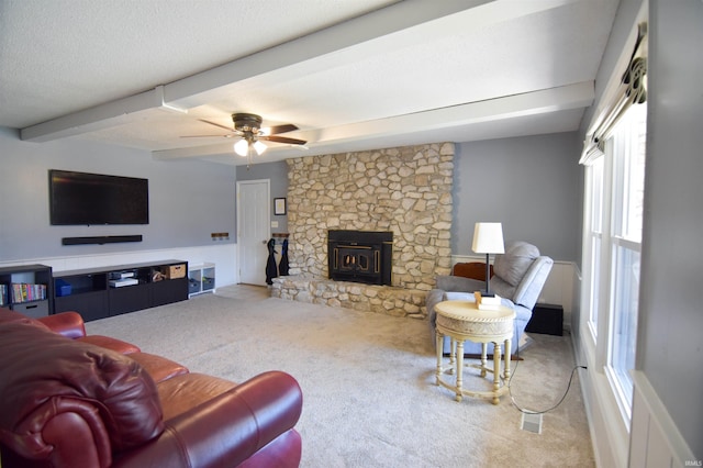 carpeted living room with beam ceiling, a textured ceiling, a stone fireplace, and a ceiling fan