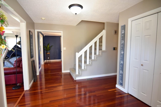 entryway with stairs, wood finished floors, baseboards, and a textured ceiling